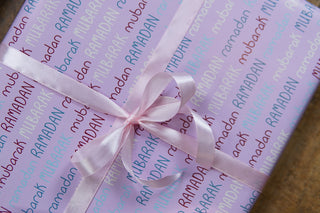 Gift wrap with pink ribbon on a pink background with 'Ramadan Mubarak' text