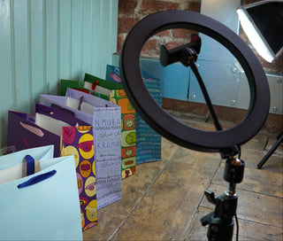 Ring light on a stand with colorful ramadan and eid bags and boxes in the background